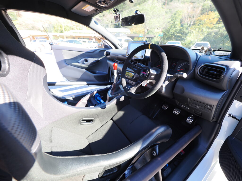 GRヤリスの運転席の画像。バックスキン巻のハンドル。社外品クイックシフター、ブリッドのバケットシート、トヨタ純正ロールバーが写っている。