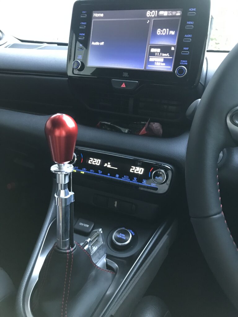 A long shift lever standing upright on the center console, with a red shift knob at its tip.