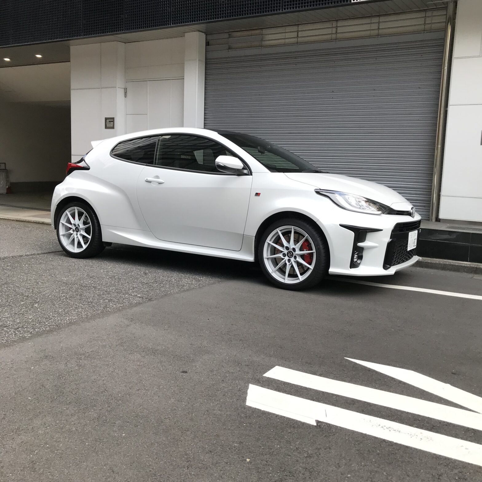 Une Toyota GR Yaris blanche est stationnée devant un immeuble en béton.